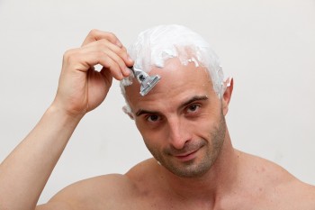 Young man shaving his head with razor blade